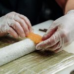 Close-up of hands making sushi with salmon and rice on a bamboo mat, showcasing precision and detail.